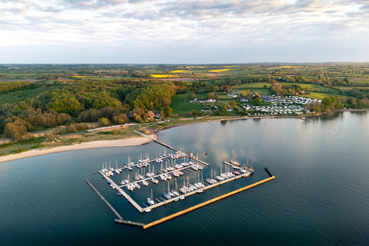Aerial view of Bockholmwik marina with sailboats moored at piers a sandy beach and a campsite surrounded by dense green forests Munkbrarup Schleswig Holstein Germany. Aerial view of Bockholmwik marina with sailboats moored at piers a sandy beach and a campsite surrounded by dense green forests Munkbrarup Schleswig Holstein Germany.
