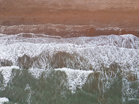Aerial view of waves crashing onto the reddish sand of the coast at Paignton Devon United Kingdom.