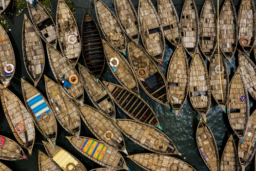 Aerial view of numerous wooden boats packed closely together on the water featuring textured wooden decks lifebuoys and colorful tarps in Dhaka Dhaka Division Bangladesh.