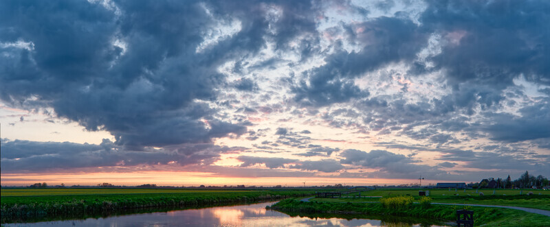View of polder Spanbroek with a calm canal reflecting a dramatic sunset sky over green fields Spanbroek North Holland Netherlands.