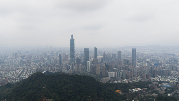 Aerial view of Taipei 101 skyscraper rising above the urban skyline with a lush green hill in the foreground under a hazy sky Taipei Taiwan.