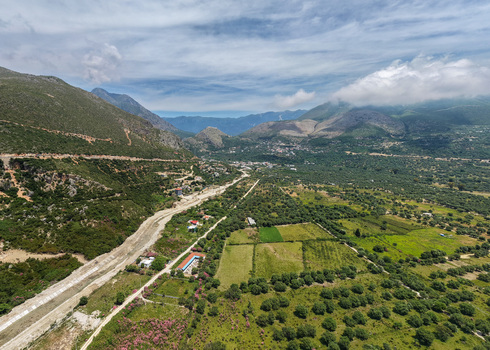 Aerial view of lush green valley with olive groves a dry riverbed and rugged mountains under a cloudy sky in Borsh Vlore County Albania. Aerial view of lush green valley with olive groves a dry riverbed and rugged mountains under a cloudy sky in Borsh Vlore County Albania.