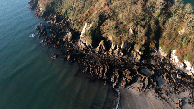 Aerial view of the rugged rocky cliffs and sandy beach at Mothecombe with calm sea waves and winter sunlight on the coastal landscape Mothecombe Devon United Kingdom. Aerial view of the rugged rocky cliffs and sandy beach at Mothecombe with calm sea waves and winter sunlight on the coastal landscape Mothecombe Devon United Kingdom.