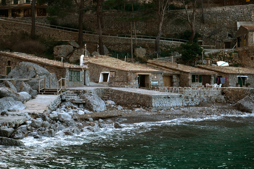 View of stone houses along the rocky coastline with pine trees and calm sea Mallorca Balearic Islands Spain.