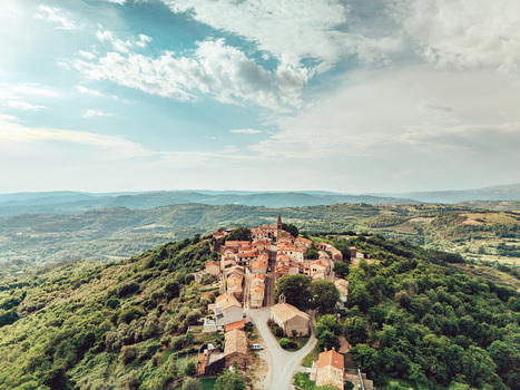 Aerial view of the historic hilltop village of Draguc with traditional stone houses and a church tower surrounded by lush green hills in Draguc Istria County Croatia.