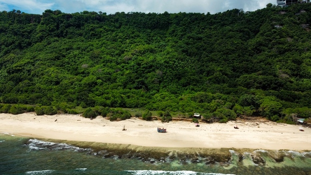 Aerial view of Pantai Nunggalan featuring a pristine sandy beach a shipwreck on the shore and lush green cliffs rising above the coastline in Kecamatan Kuta Selatan Bali Indonesia.