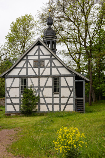 View of the Hennebergisches Museum Kloster Vessra a historic half timbered building with a small steeple surrounded by green trees and yellow flowers Kloster Vessra Thuringen Germany. View of the Hennebergisches Museum Kloster Vessra a historic half timbered building with a small steeple surrounded by green trees and yellow flowers Kloster Vessra Thuringen Germany.