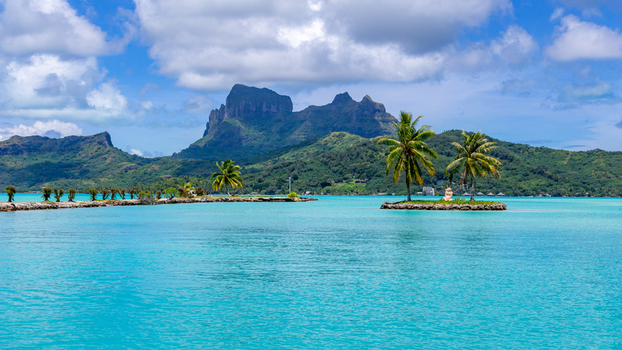 View of the turquoise lagoon and Mount Otemanu with palm trees on a small island in Bora Bora Leeward Islands French Polynesia.