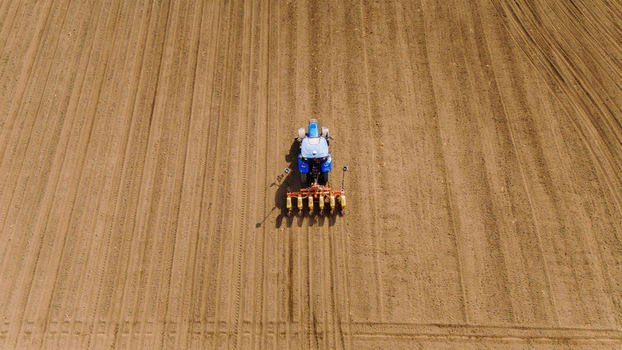 Aerial view of a blue tractor carving neat lines into the soft brown earth preparing the vast fields for planting Sremska Mitrovica Vojvodina Serbia. Aerial view of a blue tractor carving neat lines into the soft brown earth preparing the vast fields for planting Sremska Mitrovica Vojvodina Serbia.