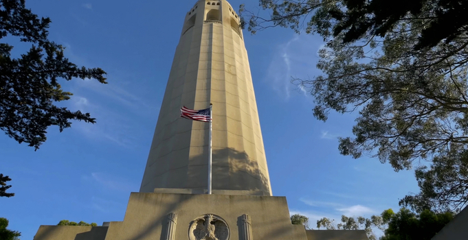 View of Coit Tower with the American flag flying against a clear blue sky in San Francisco California United States. View of Coit Tower with the American flag flying against a clear blue sky in San Francisco California United States.