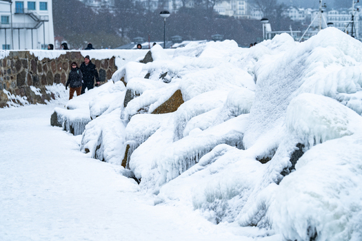 View of the snow covered breakwater and icy rocks near the Molenfeuer Sassnitz with people walking along the path in Sassnitz Mecklenburg Vorpommern Germany.