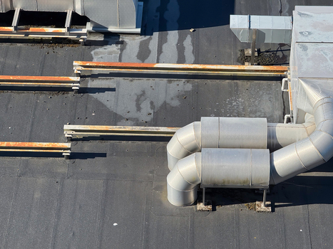 Aerial view of industrial HVAC ductwork and rusted metal supports on a flat rooftop in Leeuwarden Friesland Netherlands.