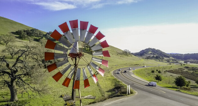 Aerial view of a red and white windmill set against rolling hills with oak trees and a winding road in Santa Barbara California United States.
