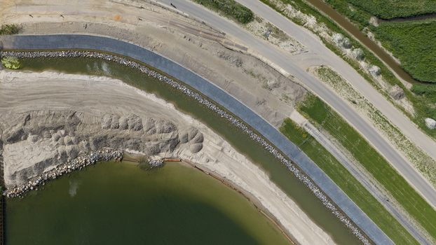 Aerial view of a dike construction site featuring a reinforced embankment sandy shoreline and a nearby road in Uitdam North Holland Netherlands.