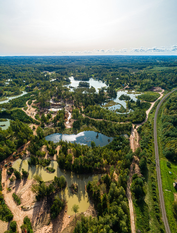 Aerial view of a landscape featuring multiple small ponds lush green forests winding dirt paths and a railway line stretching through the countryside in Latvia. Aerial view of a landscape featuring multiple small ponds lush green forests winding dirt paths and a railway line stretching through the countryside in Latvia.