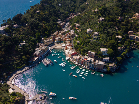 Aerial view of Portofino harbor with colorful buildings luxury yachts and lush green hills under bright sunlight in Portofino Liguria Italy.