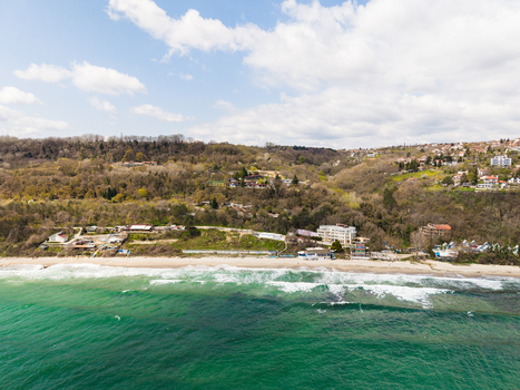 Aerial view of Fichoza Beach Veteran with the sandy shoreline turquoise Black Sea waters and forested hills with residential buildings in Varna Varna Bulgaria. Aerial view of Fichoza Beach Veteran with the sandy shoreline turquoise Black Sea waters and forested hills with residential buildings in Varna Varna Bulgaria.