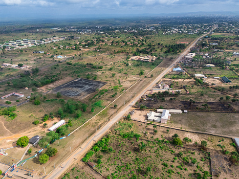Aerial view of a straight road dissecting a vibrant green and brown landscape featuring scattered buildings and a dark pond Elu Abia Nigeria. Aerial view of a straight road dissecting a vibrant green and brown landscape featuring scattered buildings and a dark pond Elu Abia Nigeria.