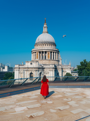 View of a person in a striking red dress on a rooftop gazing at the majestic St. Paul s Cathedral under a clear blue sky London England United Kingdom. View of a person in a striking red dress on a rooftop gazing at the majestic St. Paul s Cathedral under a clear blue sky London England United Kingdom.