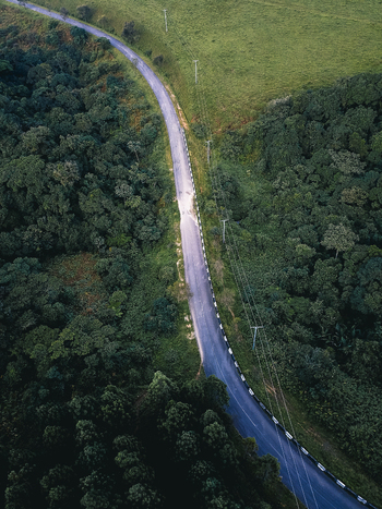 Aerial view of a serpentine ribbon of asphalt cutting through a verdant canopy and an emerald expanse Obudu Cross River Nigeria.