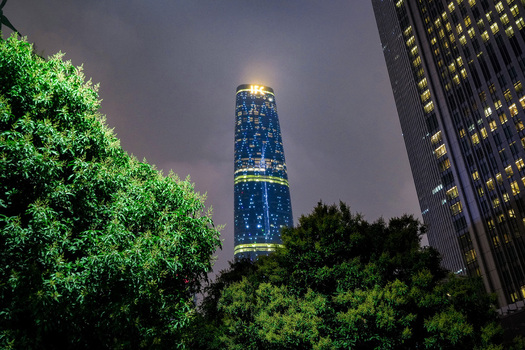Guangzhou China 24 February 2024 View of the Guangzhou International Finance Center illuminated at night framed by lush green trees and modern skyscraper architecture. Guangzhou China 24 February 2024 View of the Guangzhou International Finance Center illuminated at night framed by lush green trees and modern skyscraper architecture.