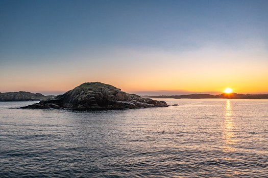Aerial view of a rocky island off the coast during a golden sunset with calm waters and a clear sky in Kincasslagh County Donegal Ireland. Aerial view of a rocky island off the coast during a golden sunset with calm waters and a clear sky in Kincasslagh County Donegal Ireland.