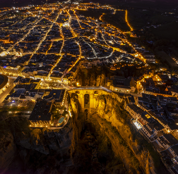 Aerial view of the illuminated Puente Nuevo bridge spanning the deep gorge in the historic town of Ronda with glowing street lights and ancient architecture in Ronda Andalusia Spain. Aerial view of the illuminated Puente Nuevo bridge spanning the deep gorge in the historic town of Ronda with glowing street lights and ancient architecture in Ronda Andalusia Spain.