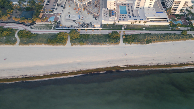Aerial view of the sandy coastline and oceanfront hotels featuring a construction site swimming pools and palm trees along the shore in Miami Beach Florida United States. Aerial view of the sandy coastline and oceanfront hotels featuring a construction site swimming pools and palm trees along the shore in Miami Beach Florida United States.