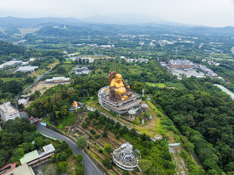 Aerial view of the large golden Buddha statue at the Fo Guang Shan Buddha Museum surrounded by lush green hills and trees in Jiuru Township Pingtung County Taiwan. Aerial view of the large golden Buddha statue at the Fo Guang Shan Buddha Museum surrounded by lush green hills and trees in Jiuru Township Pingtung County Taiwan.