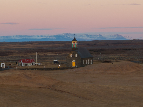 Aerial view of Hvalsneskirkja church set in a vast rural landscape with distant snow capped mountains under a soft golden hour sky in Sudurnesjabaer Iceland. Aerial view of Hvalsneskirkja church set in a vast rural landscape with distant snow capped mountains under a soft golden hour sky in Sudurnesjabaer Iceland.