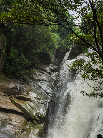 View of a powerful waterfall cascading over rugged wet rock formations surrounded by lush green foliage and trees in Jos Plateau Nigeria. View of a powerful waterfall cascading over rugged wet rock formations surrounded by lush green foliage and trees in Jos Plateau Nigeria.