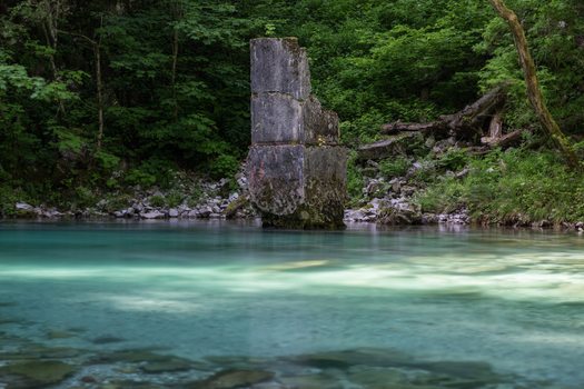 View of a stone pillar ruin standing in the turquoise waters of the Vintgar Gorge surrounded by lush green forest in Bled Radovljica Slovenia.