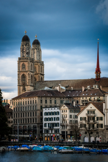 Zurich Switzerland 02 April 2023 View of the majestic Grossmünster church towers rising above the historic rooftops against a dramatic moody sky reflected in the tranquil waters below. Zurich Switzerland 02 April 2023 View of the majestic Grossmünster church towers rising above the historic rooftops against a dramatic moody sky reflected in the tranquil waters below.