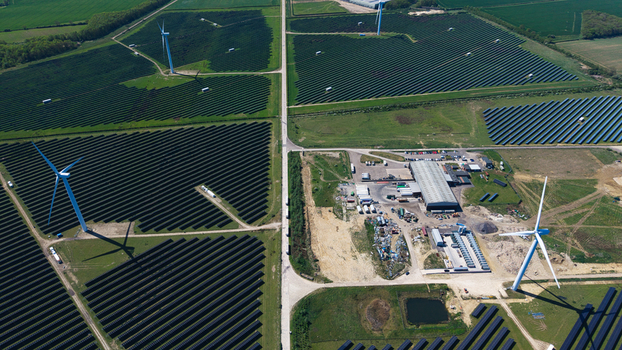 Aerial view of Chelveston Wind Farm featuring wind turbines and vast solar panel arrays across green fields in Wellingborough England United Kingdom. Aerial view of Chelveston Wind Farm featuring wind turbines and vast solar panel arrays across green fields in Wellingborough England United Kingdom.