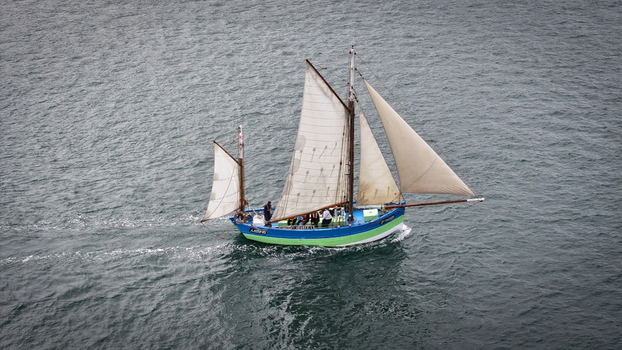 Aerial view of a vibrant sailing boat cutting through the dark textured waters near the coastline Carantec Brittany France.
