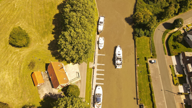 Aerial view of boats moored along a canal next to a house with a red roof and lush green surroundings in Saint Omer Hauts de France France. Aerial view of boats moored along a canal next to a house with a red roof and lush green surroundings in Saint Omer Hauts de France France.