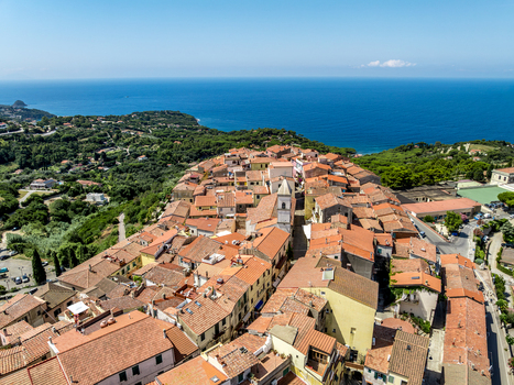 Aerial view of the historic town of Capoliveri featuring terracotta rooftops narrow streets and a church tower overlooking the Mediterranean Sea in Capoliveri Tuscany Italy.