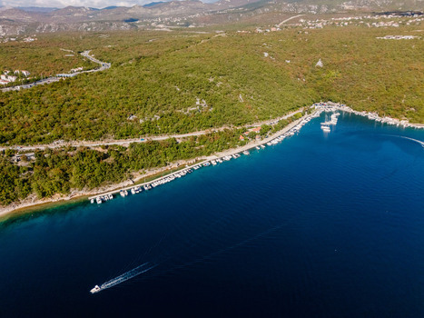 Aerial view of the Krk Bridge spanning the blue Adriatic Sea near the lush coastline of Smrika featuring small boats moored along the shore in Smrika Primorje Gorski Kotar Croatia. Aerial view of the Krk Bridge spanning the blue Adriatic Sea near the lush coastline of Smrika featuring small boats moored along the shore in Smrika Primorje Gorski Kotar Croatia.
