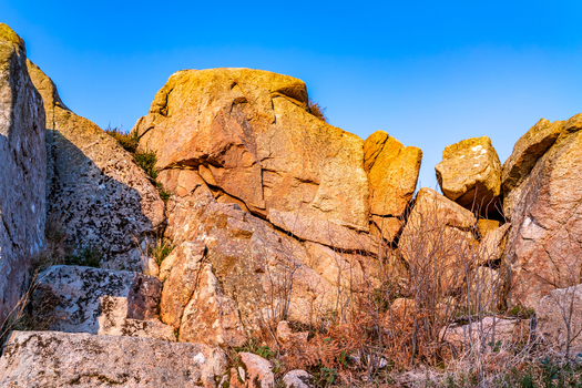View of the historic Kincasslagh Mass Rock featuring rugged granite boulders weathered stone surfaces and sparse vegetation under a clear blue sky in Kincasslagh County Donegal Ireland. View of the historic Kincasslagh Mass Rock featuring rugged granite boulders weathered stone surfaces and sparse vegetation under a clear blue sky in Kincasslagh County Donegal Ireland.