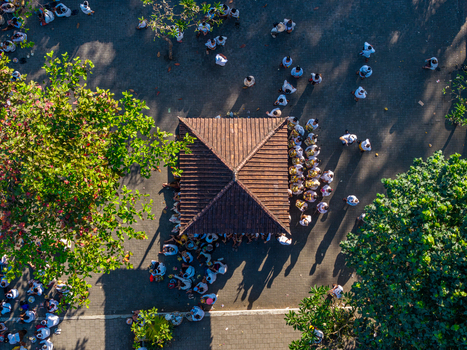 Aerial view of the Ngelarung Sea Offering Ceremony at Pura Segara Goa Lawah with people gathered around a temple structure lush trees and long shadows in Dawan Bali Indonesia.