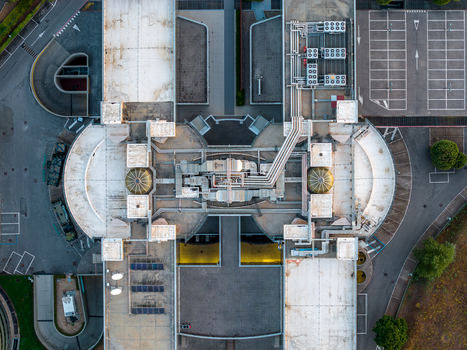 Aerial view of a modern datacenter facility featuring complex rooftop HVAC systems geometric building layout and adjacent parking areas in Settecamini Lazio Italy.