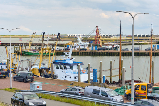 Den Oever Netherlands 18 May 2026 View of fishing vessels docked at the Machinefabriek wharf for renovation with parked cars along the harbor quay under a cloudy sky.