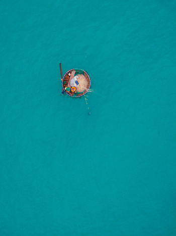 Aerial view of a traditional round basket boat with a fisherman and fishing nets floating on calm turquoise water in Vietnam. Aerial view of a traditional round basket boat with a fisherman and fishing nets floating on calm turquoise water in Vietnam.