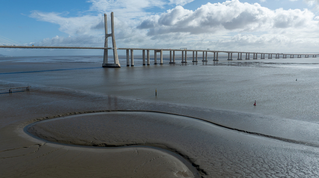 Aerial view of the Vasco da Gama Bridge spanning the Tagus River with mudflats at low tide under a blue sky with clouds in Lisboa Portugal.