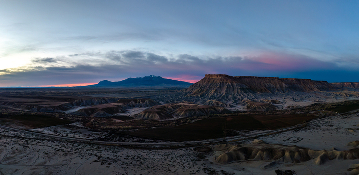 Aerial view of the desert landscape near Caineville featuring rugged mesas badlands and a winding road under a colorful sunset sky in Caineville Utah United States.