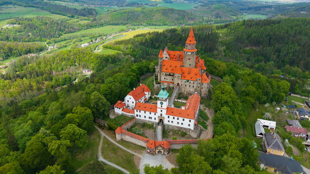 Aerial view of Bouzov Castle with its iconic red roofs and tall tower surrounded by dense green forests and rolling hills Bouzov Olomoucky kraj Czechia. Aerial view of Bouzov Castle with its iconic red roofs and tall tower surrounded by dense green forests and rolling hills Bouzov Olomoucky kraj Czechia.
