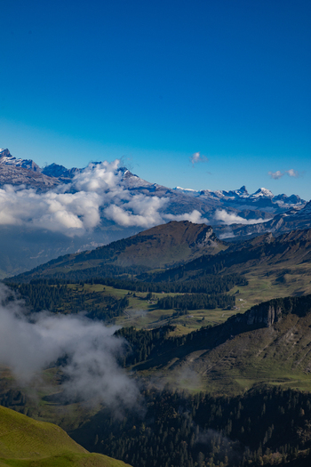 Aerial view of the Swiss Alps with snow capped peaks rolling green valleys dense pine forests and clouds drifting over the landscape in Airolo Ticino Switzerland. Aerial view of the Swiss Alps with snow capped peaks rolling green valleys dense pine forests and clouds drifting over the landscape in Airolo Ticino Switzerland.