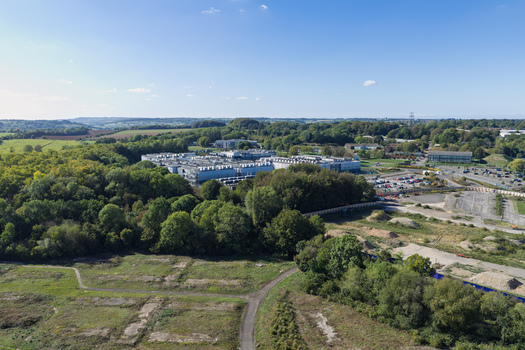 Aerial view of a large data center complex nestled within a dense forest featuring industrial buildings parking areas and surrounding green landscape in the United Kingdom.
