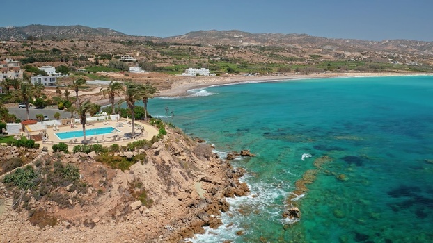 Aerial view of a swimming pool on a rocky cliff overlooking the turquoise Mediterranean Sea with palm trees and coastal hills in Cyprus. Aerial view of a swimming pool on a rocky cliff overlooking the turquoise Mediterranean Sea with palm trees and coastal hills in Cyprus.