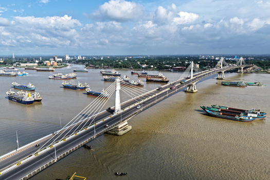 Aerial view of the Shah Amanat Bridge spanning the Karnaphuli River with numerous cargo ships navigating the waterway under a bright sky in Chattogram Chittagong Division Bangladesh.